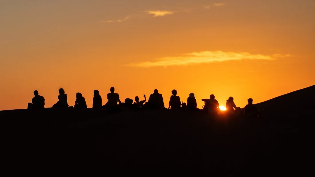 Un groupe assis sur une dune au coucher du soleil, dans le désert marocain